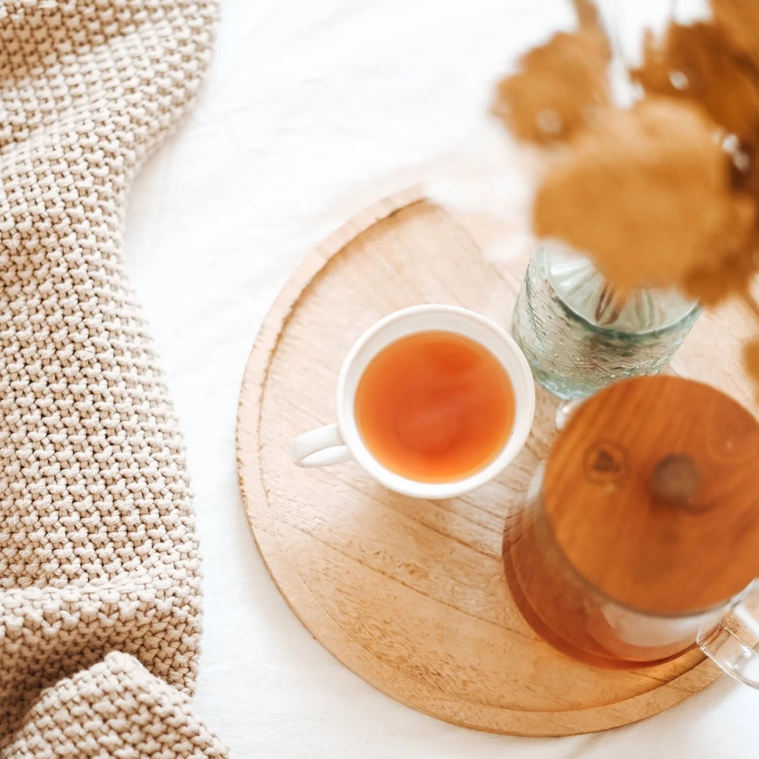 Teacup on a wooden coaster with a textured blanket and dried flowers in the background